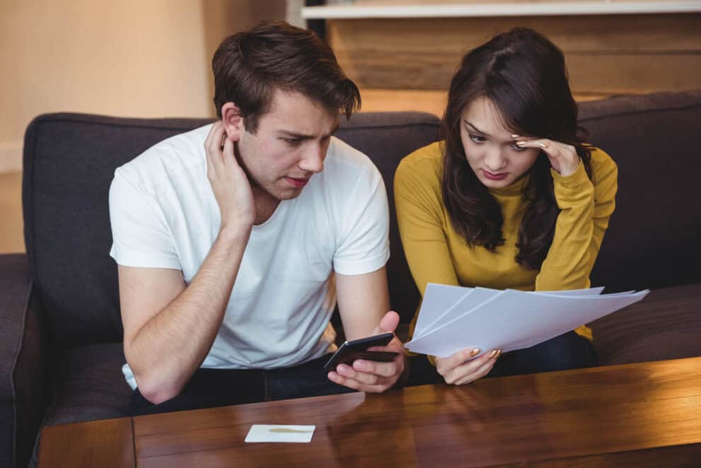 Couple sitting on sofa discussing with documents in living room at home