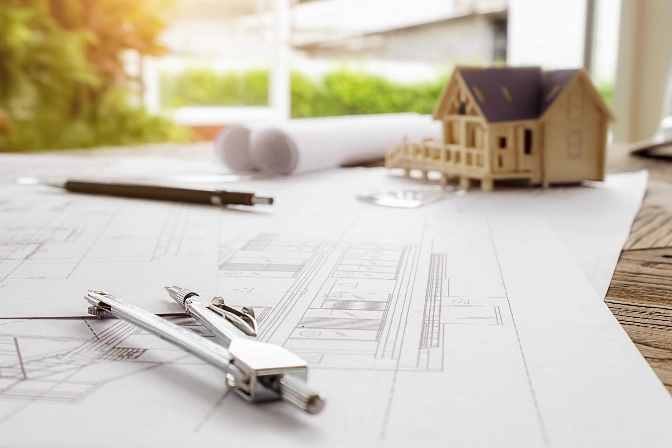 Close up of an architect's desk with schematics of a property and a small model of said property.